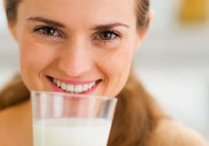 Mujer sosteniendo un vaso de leche fresca y sonriendo